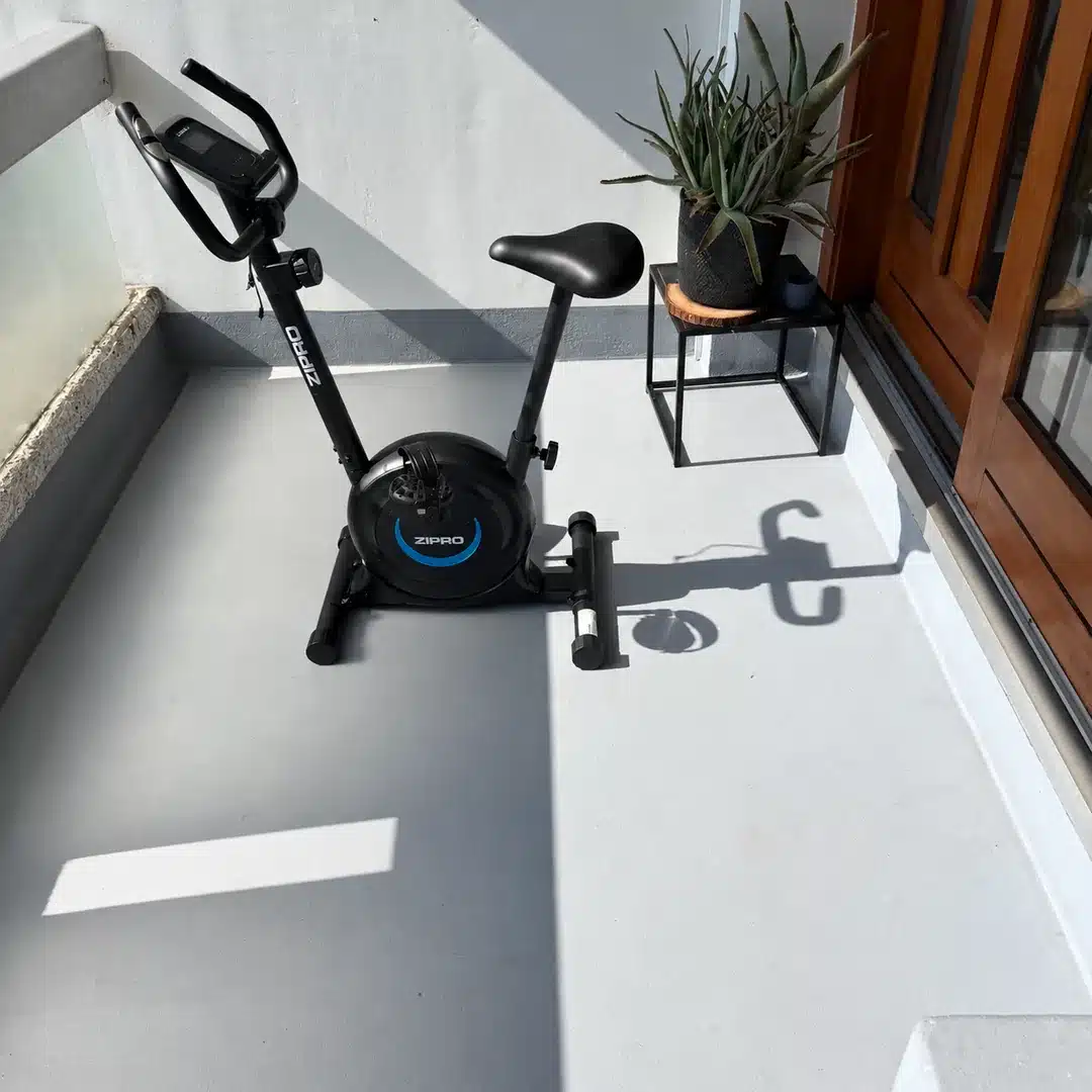 Sol de balcon après nettoyage, avec un vélo d’appartement et une plante en pot.