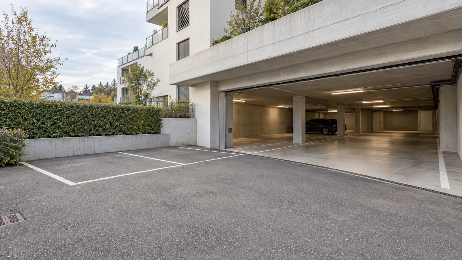 Places de parc extérieures devant l’entrée d’un parking couvert en résidence.